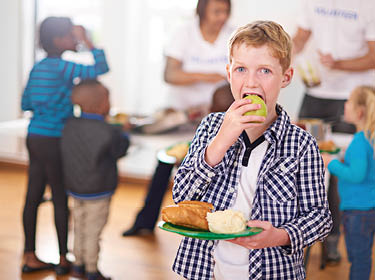  Student biting an apple while carrying a plate of food.